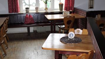Un restaurante con mesas y sillas de madera, un banco y un ventanal con cortinas rojas.