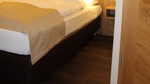 A hotel room with a wooden headboard, a bed with white linens, two yellow pillows, and a nightstand with a lamp. - Hotel Brauereigasthof Amberger (Kosching)
