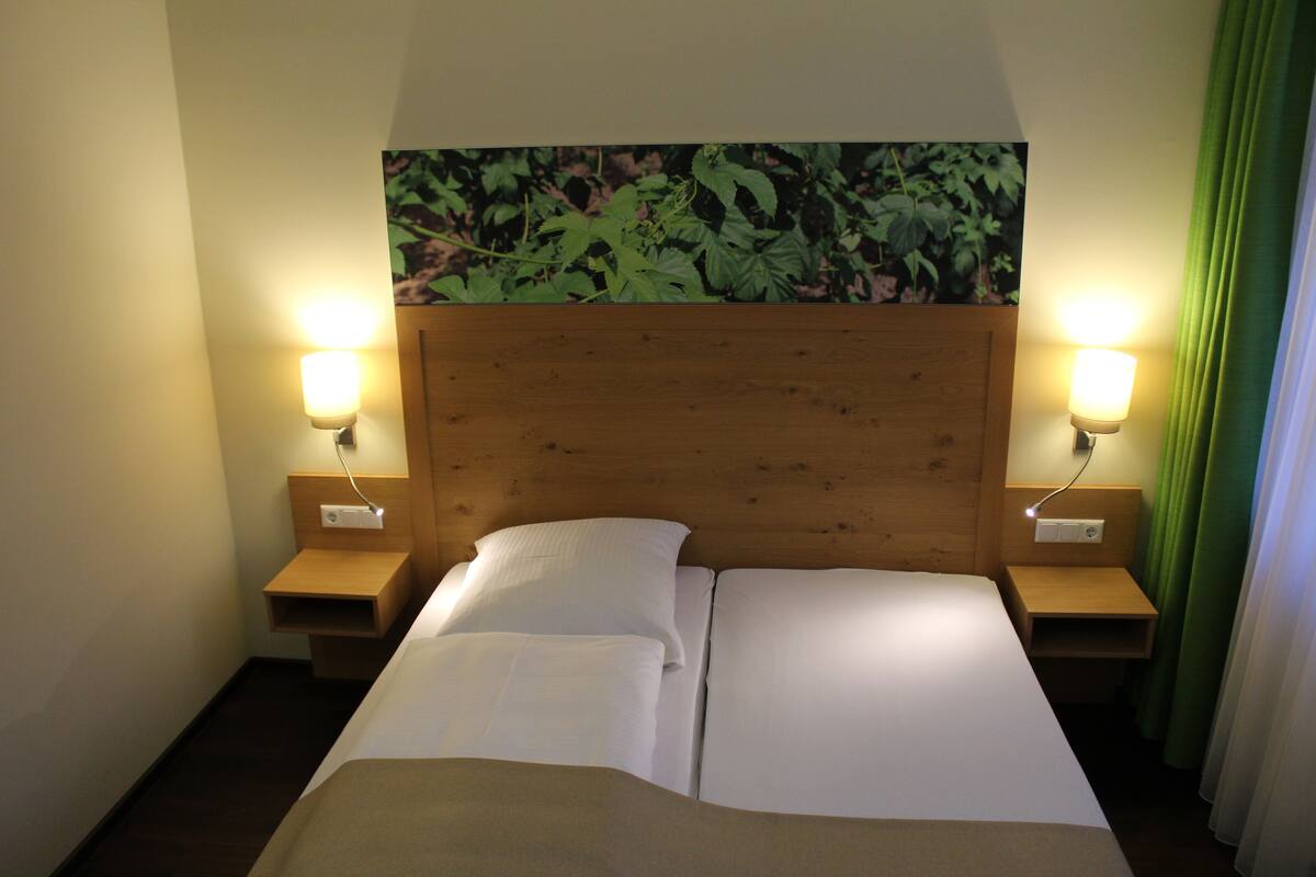 Ein Hotelzimmer mit einem hölzernen Kopfteil, zwei Nachttischen mit Lampen, einem Bett mit weißen Leinen und einem grünen Vorhang.