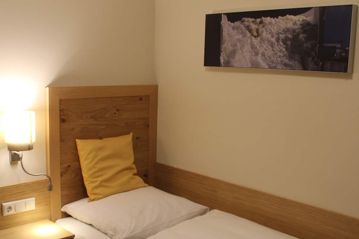 Ein Einzelbett mit Holz Kopfteil, ein Nachttisch mit Lampe und ein gerahmtes Bild an der Wand.
