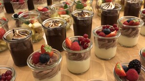 A variety of desserts in glass jars, some with whipped cream and berries, arranged on a wooden table. - Hotel Brauereigasthof Amberger (Kosching)