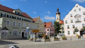 A historic town square with buildings, a clock tower, and directional signs. - Hotel Brauereigasthof Amberger (Kosching)