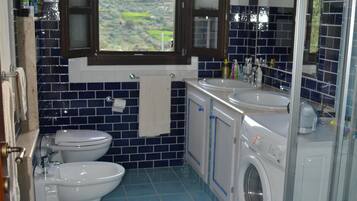 Ein kleines Badezimmer mit Waschmaschine, zwei Toiletten, einem Waschbecken und einer Dusche.