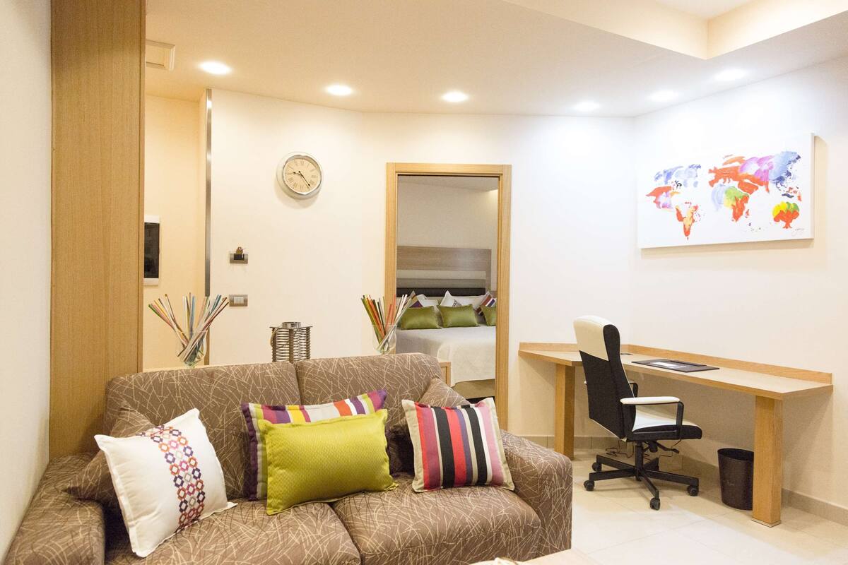Ein moderner Arbeitsraum mit einem braunen, gemusterten Sofa, einem Holztisch und einer farbenfrohen Weltkarte an der Wand.