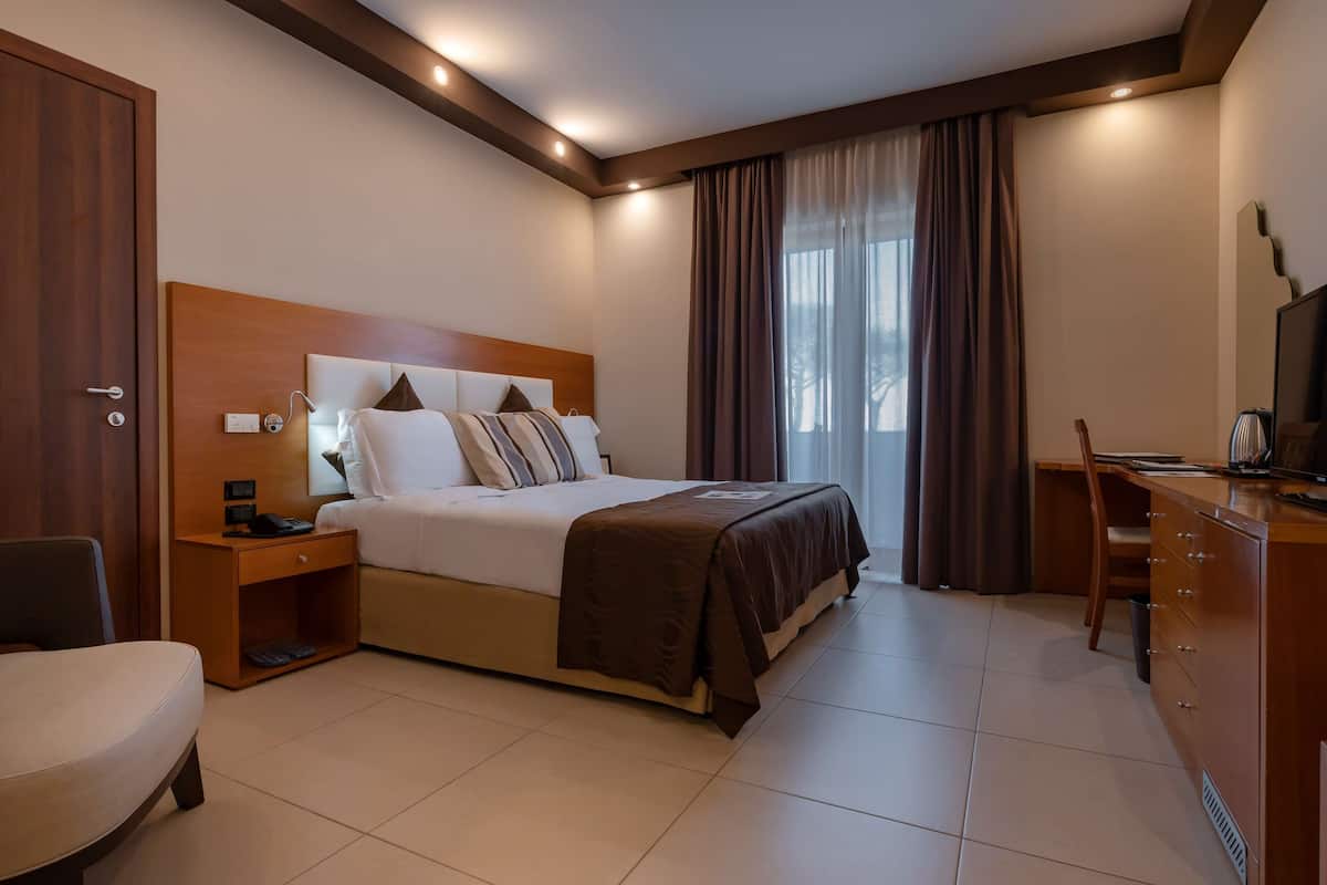 Ein Hotelzimmer mit einem großen Bett, einem Schreibtisch, einem Sessel und einem Fernseher.