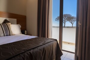 Habitación de hotel con una cama grande, cabecera de madera y vista a un árbol por la ventana.