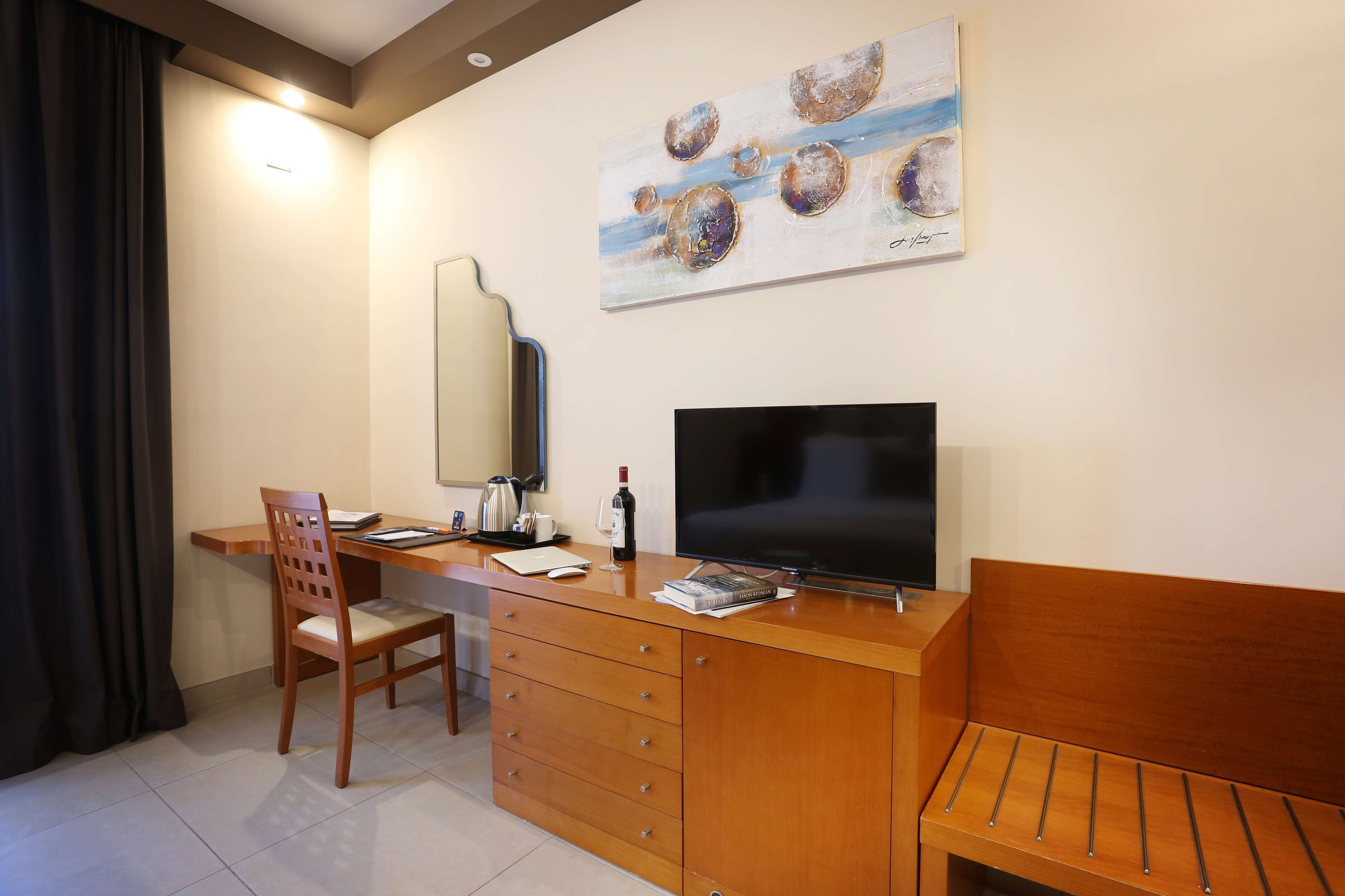 Habitación de hotel con un escritorio de madera, televisor, silla, sofá y un cuadro en la pared.