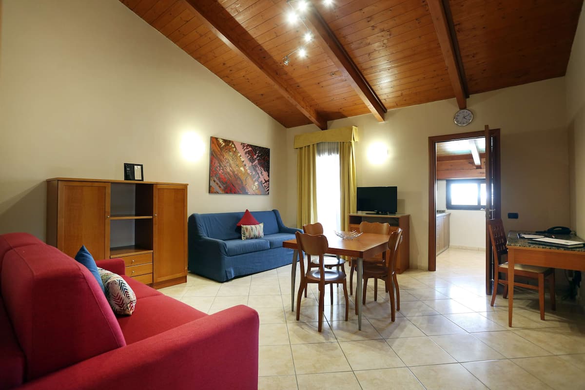 Ein Wohnzimmer mit einem roten Sofa, einem blauen Sofa, einem Holzesstisch mit Stühlen, einem Holzschrank und einem Bild an der Wand.