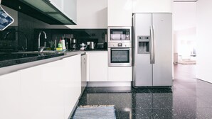 Eine moderne Küche mit weißen Schränken, einem Edelstahlkühlschrank, einer Mikrowelle und einer Kaffeemaschine.