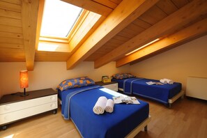 A room with two beds, a nightstand, a lamp, and a skylight.