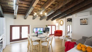 A modern living room with a dining area, wooden beams on the ceiling, a red chair, and a table with oranges. - Singular Stays A. San Vicente IV (Valencia)