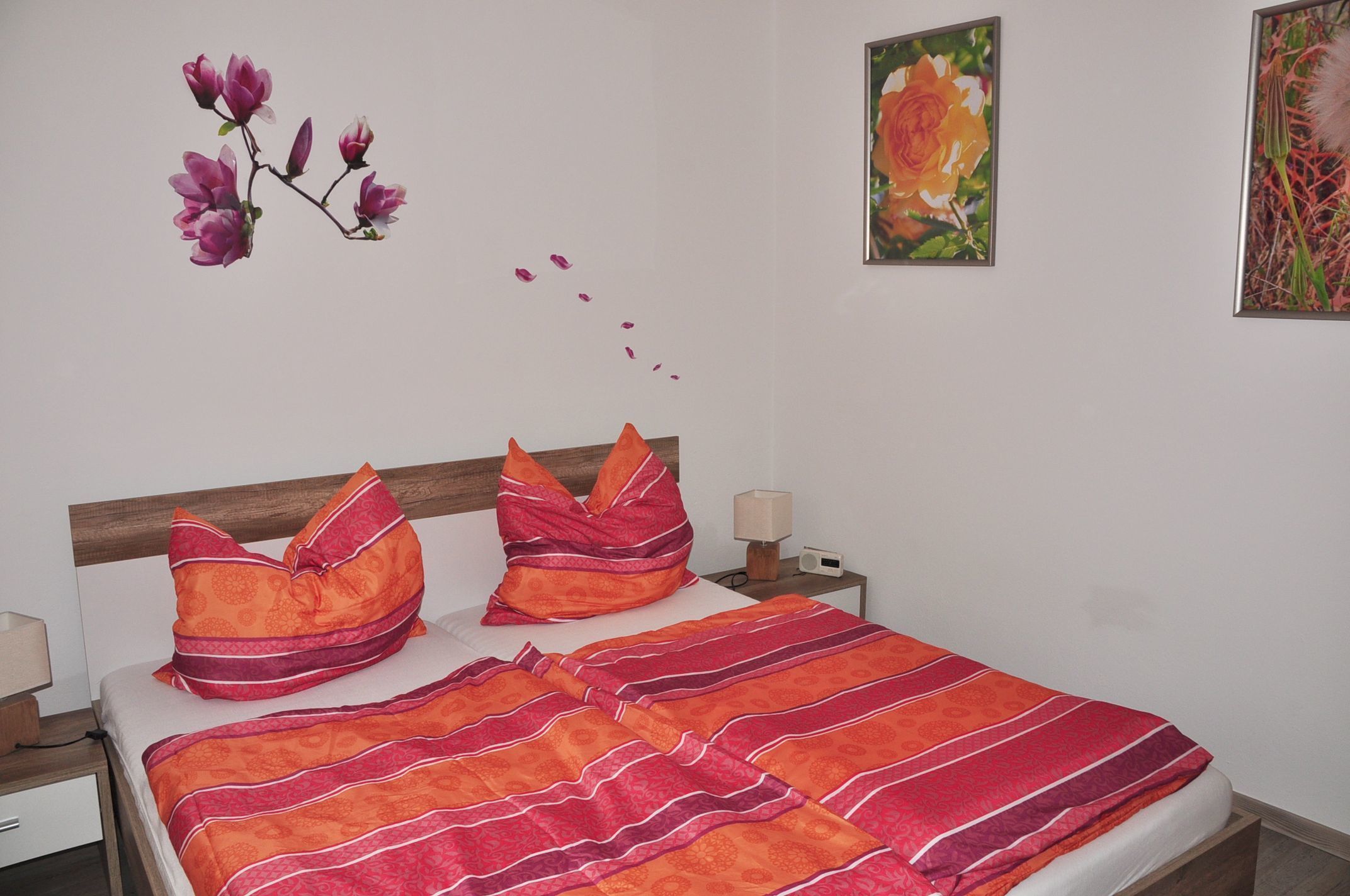 A bed with a striped blanket, two pillows, a nightstand with a lamp, and a wall with a flower painting.