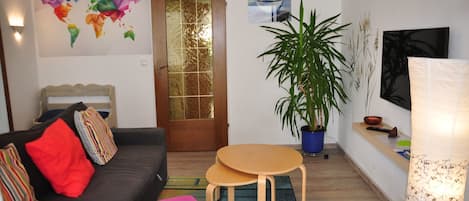 A living room with a sofa, a small table, a potted plant, and a wall-mounted TV.