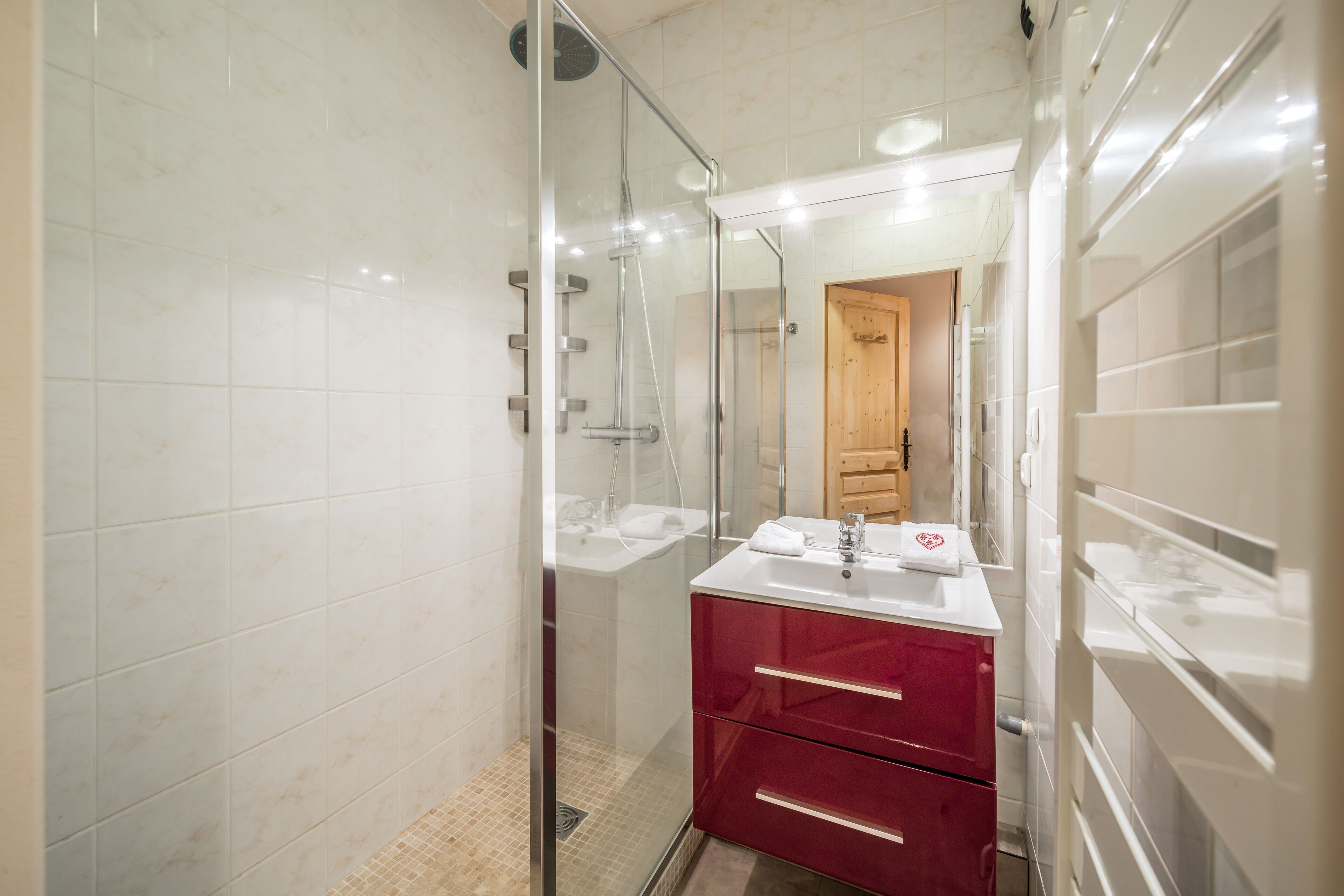 Ein Badezimmer mit einer Duschkabine, einem weißen Waschbecken und einer Holztür im Hintergrund.