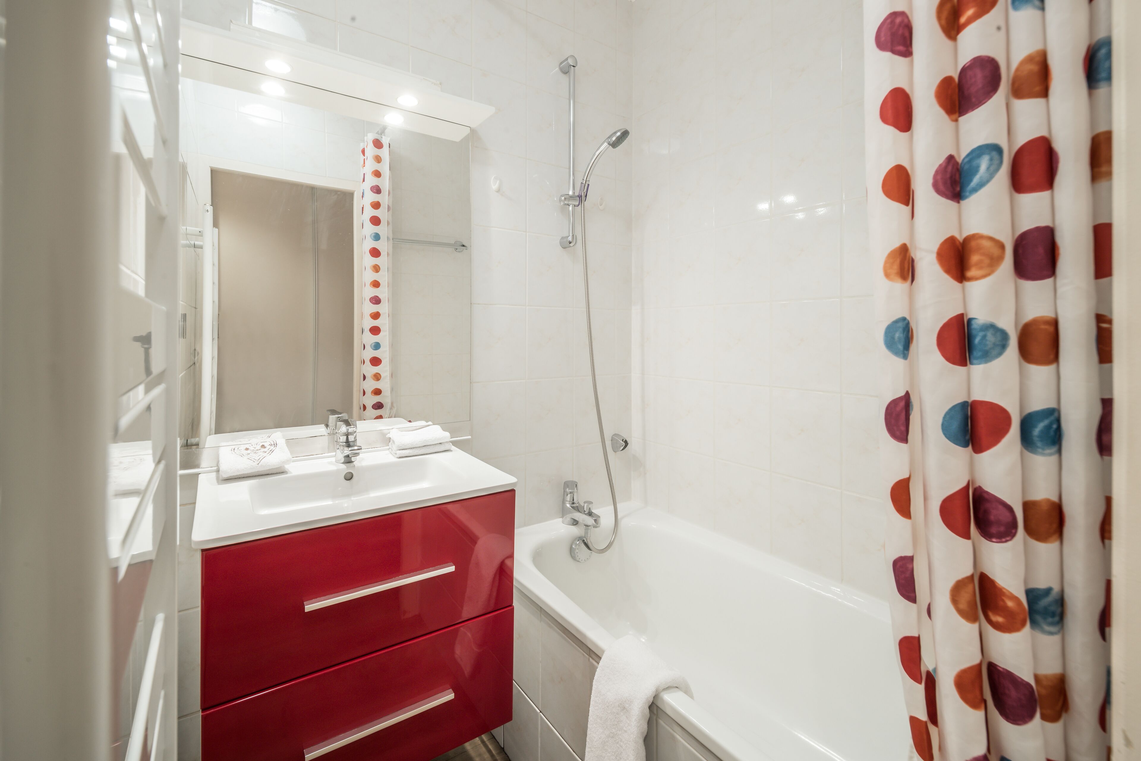 A bathroom with a white sink, red cabinet, and a bathtub.