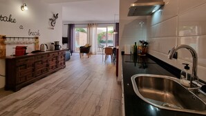 Une cuisine moderne avec un plan de travail noir, un évier en acier inoxydable et un coin repas comprenant une chaise et une table en osier.