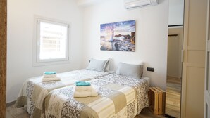 Une chambre avec deux lits, une fenêtre, un climatiseur et un tableau au mur.