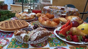 Un tavolo con diversi pasticcini, frutta e una brocca di bevanda rossa, su una tovaglia colorata.