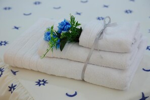 A stack of white towels with a floral arrangement and a ribbon, placed on a bed with a white and blue star-patterned bedspread. - Il Melograno (Agrigento)