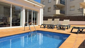 A swimming pool with lounge chairs, a glass door entrance, and a building with balconies. - Agi Las Acacias 2401 Apartamento for rent in Roses Girona. (Rosas / Roses)