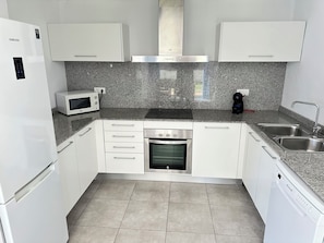 A compact kitchen with white cabinets, a built-in microwave, a stainless steel oven, and a dishwasher.