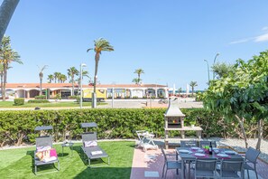 A patio area with lounge chairs, a barbecue grill, and a view of a commercial building with palm trees.