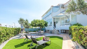 A modern house with a patio area featuring a lawn, outdoor furniture, and a staircase leading to a second floor.