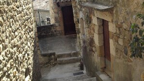 A narrow stone pathway leading to a building with a tiled roof and a wooden door.