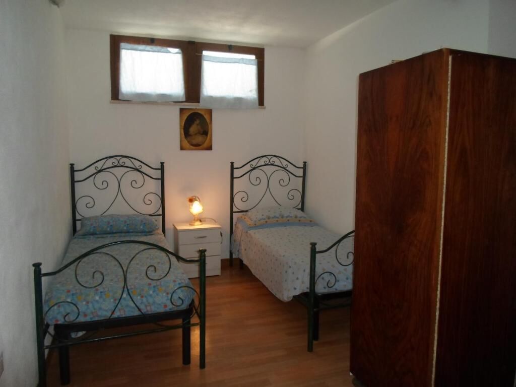 A bedroom with two metal-framed beds, a wooden wardrobe, a nightstand, and a small window.