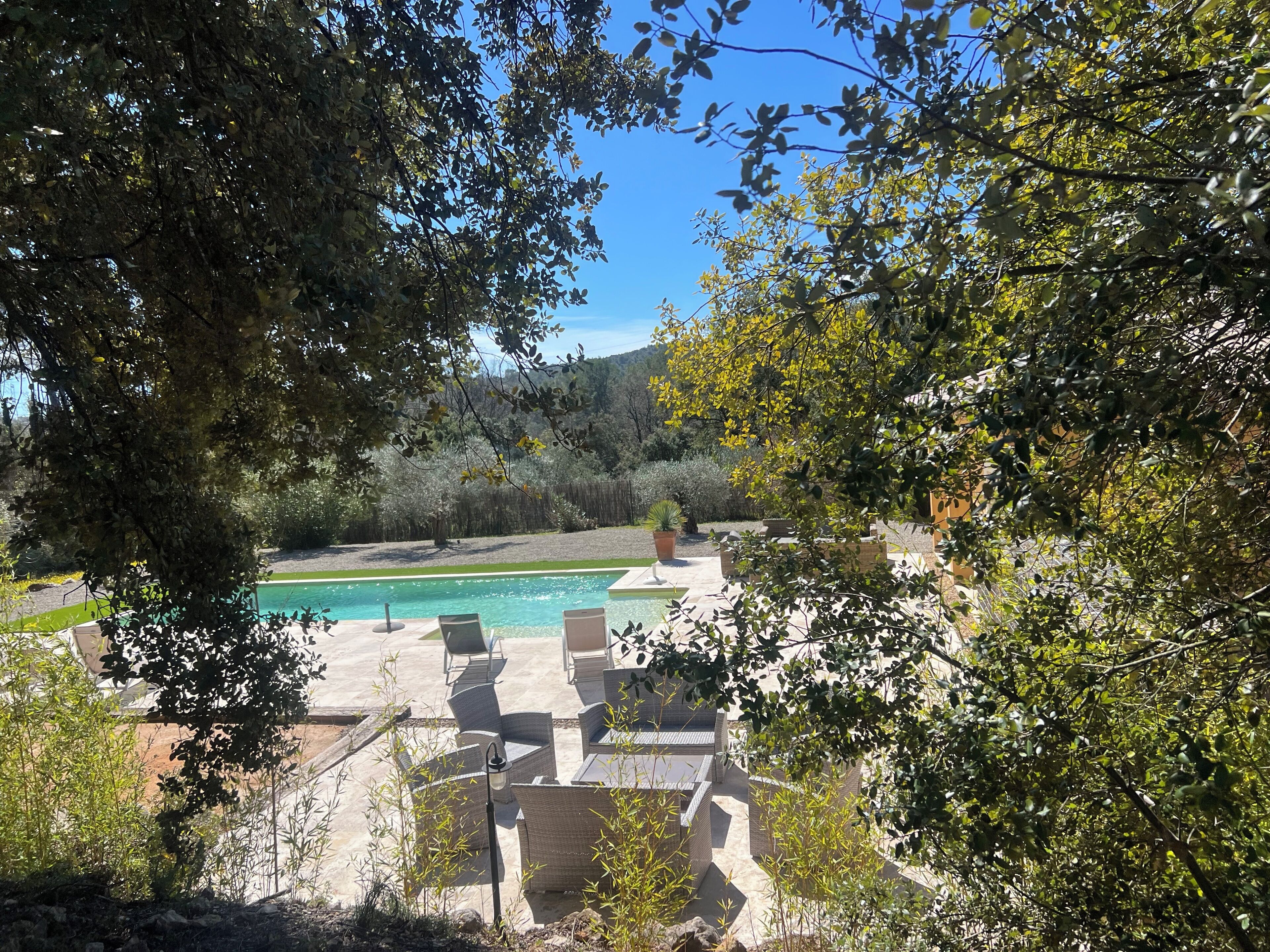 A pool area with lounge chairs, surrounded by trees and a view of a hilly landscape.