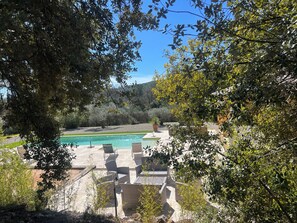 A pool area with lounge chairs, surrounded by trees and a view of a hilly landscape. - Large 200 m² house with a private garden and swimming pool (Lorgues)