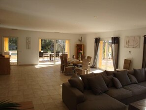 A spacious living room with a large sofa, a dining area with a table and chairs, and a sliding glass door leading to an outdoor patio. - Large 200 m² house with a private garden and swimming pool (Lorgues)