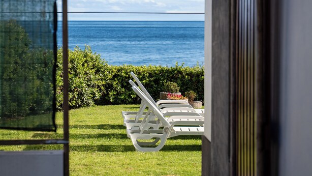 A view from a balcony overlooking a sea with lounge chairs and a well-maintained garden. - Fisherman's House Azores (São Mateus) (Angra do Heroísmo)