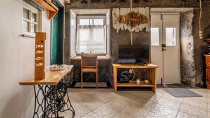 A rustic room with a wooden table, a chair, a television on a wooden stand, a fish decoration, and a stone wall. - Fisherman's House Azores (São Mateus) (Angra do Heroísmo)