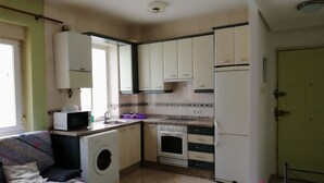 A compact kitchen with a washing machine, microwave, sink, and a small dining area with a table and sofa. - MY BLACK HOMEAWAY (León)