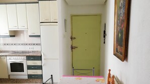 A compact kitchen with white cabinets, a built-in oven, and a dining table with a pink tablecloth. - MY BLACK HOMEAWAY (León)