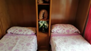 A small, cozy room with two beds, each with floral-patterned bedding and matching pillows. There is a wooden shelf with a vase of flowers and a folded blanket. - MY BLACK HOMEAWAY (León)