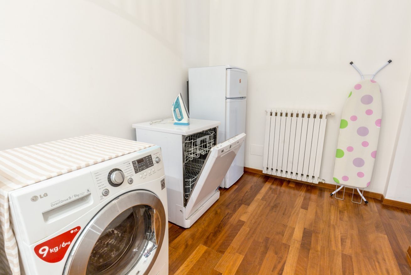 A laundry room with a washing machine, a dryer, a refrigerator, and an ironing board.