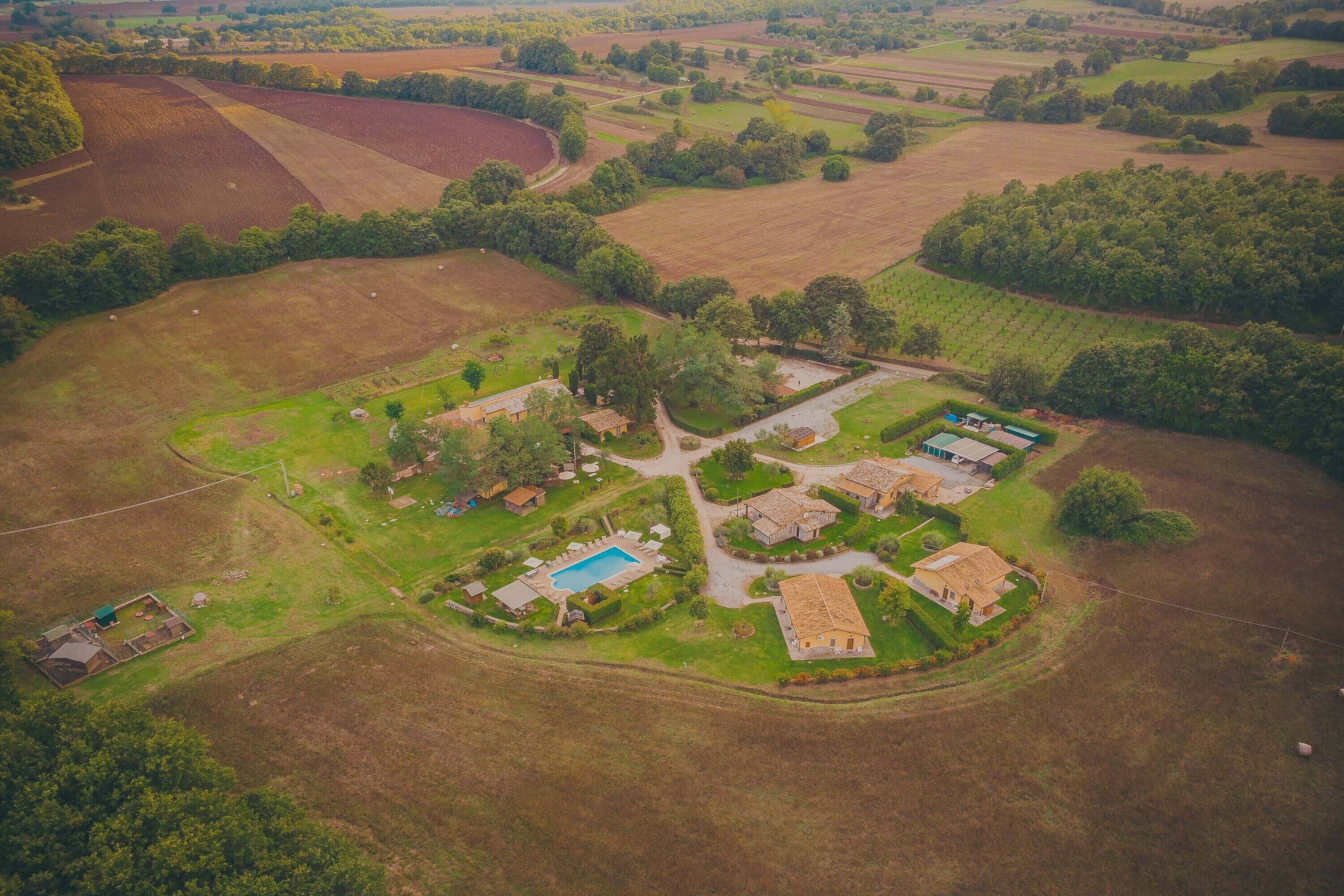 An aerial view of a rural property with multiple buildings, a swimming pool, and surrounding fields.