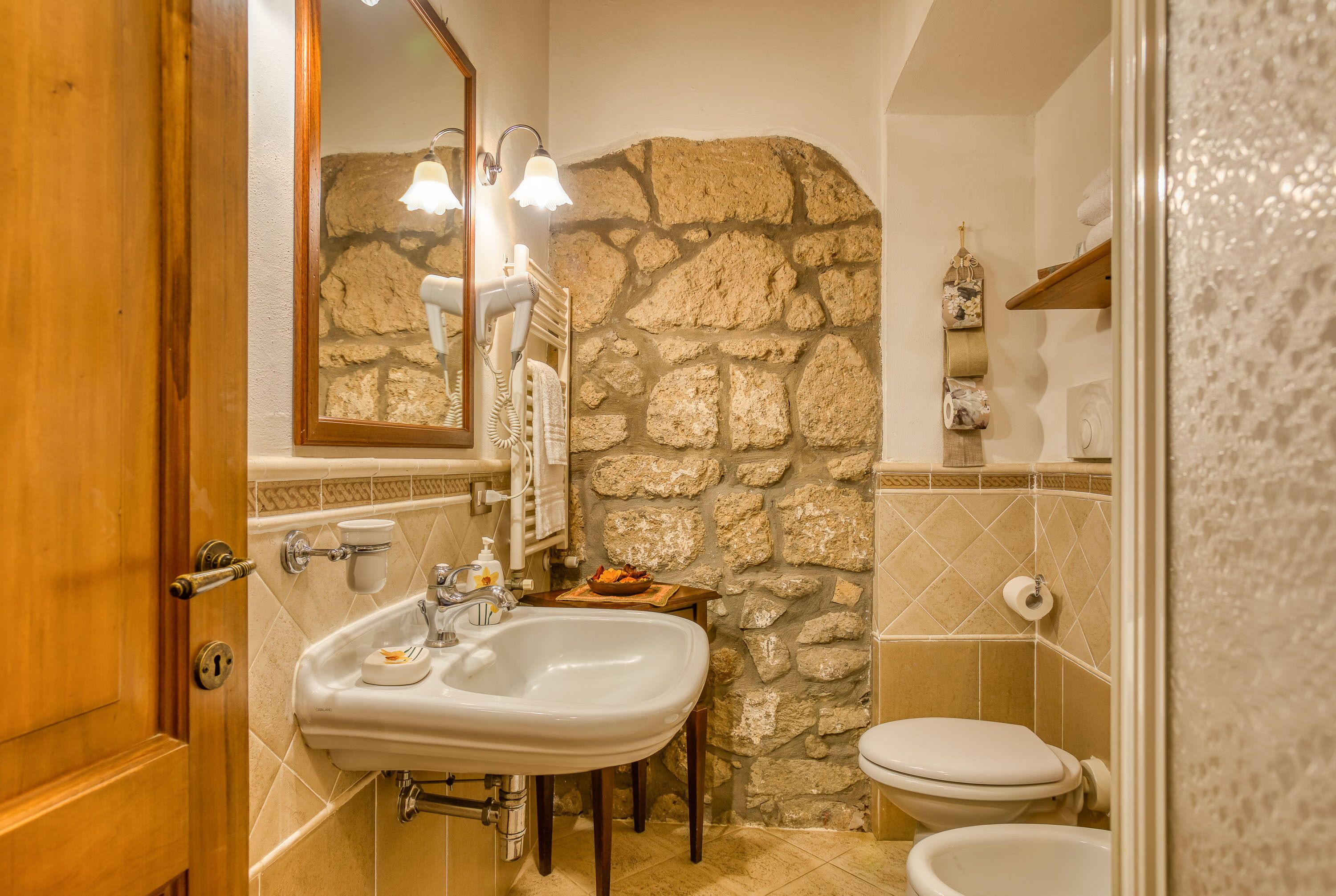 A bathroom with a stone wall, a sink, a toilet, and a mirror.