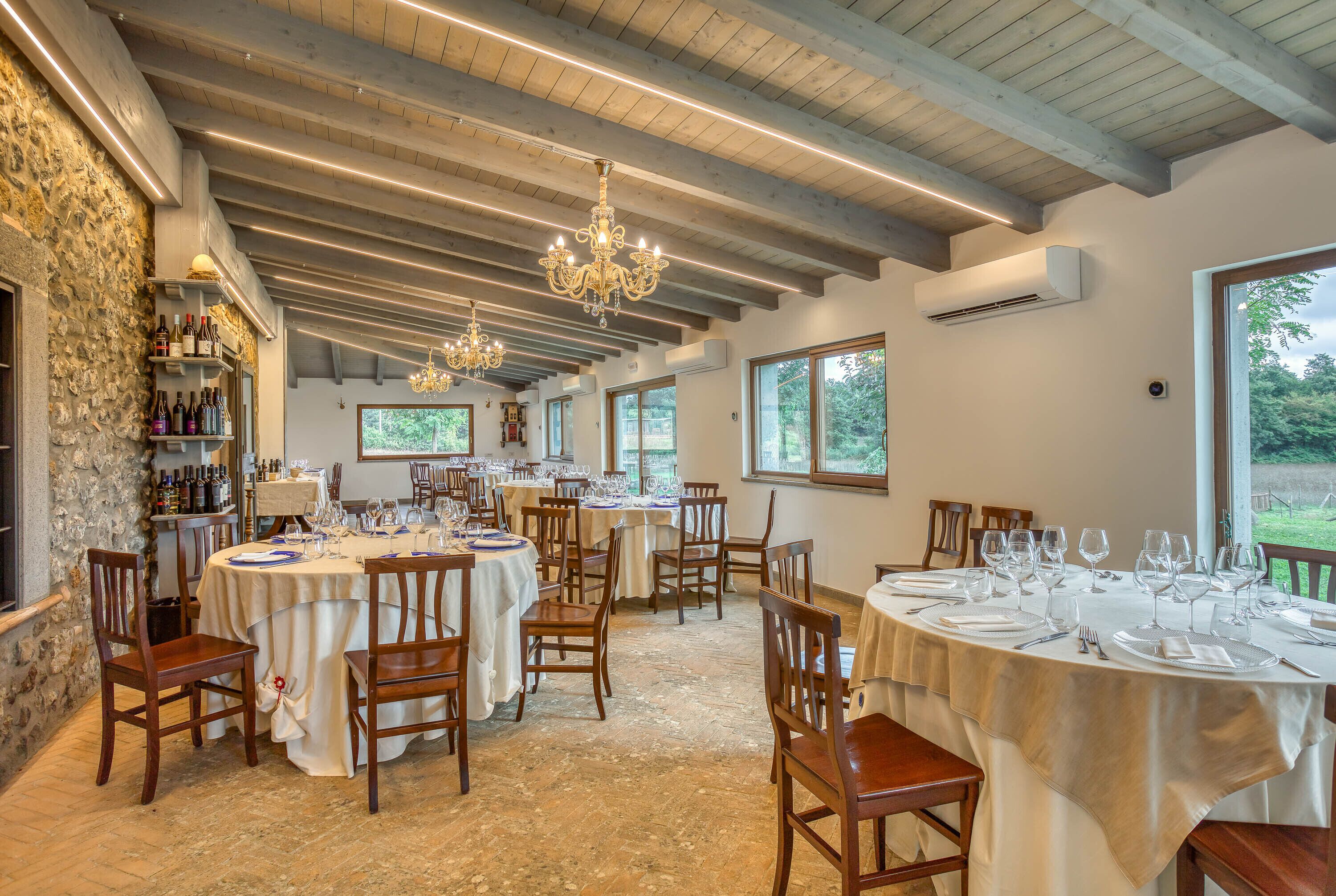 A dining area with round tables set for six, wooden chairs, and a stone wall on one side.