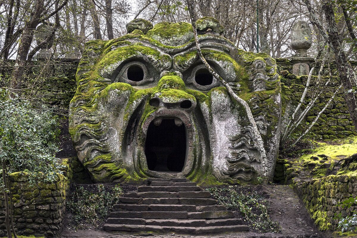 Een stenen constructie met een gebeeldhouwd gezicht, begroeid met mos, omringd door bomen.