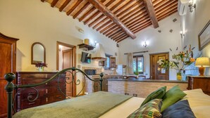A bedroom with a bed, a wooden headboard, a dresser, and a kitchen area visible through an open door. - Agriturismo Buonasera (Bagnoregio)