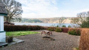 A gravel patio with a wooden bench and a bird feeder, overlooking a lake with hills in the background. - Lovely foresters cottage, amazing Loch Ness views, private beach, pets welcome (Inverfarigaig,   Loch Ness)