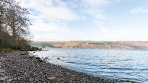 A pebbled beach with a calm lake, surrounded by trees and hills in the distance. - Lovely foresters cottage, amazing Loch Ness views, private beach, pets welcome (Inverfarigaig,   Loch Ness)