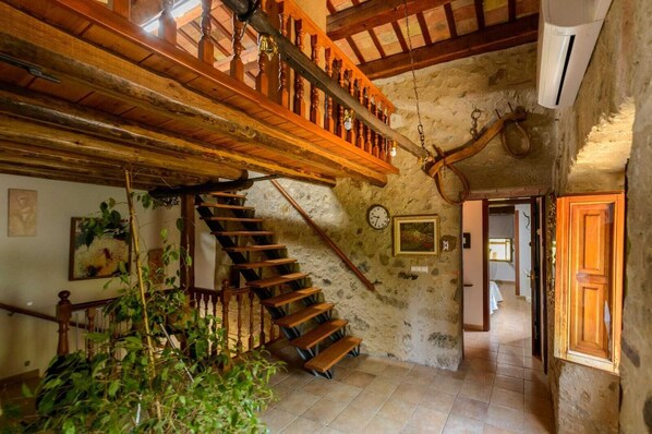 A rustic interior with a wooden staircase, stone walls, and a hanging light fixture.