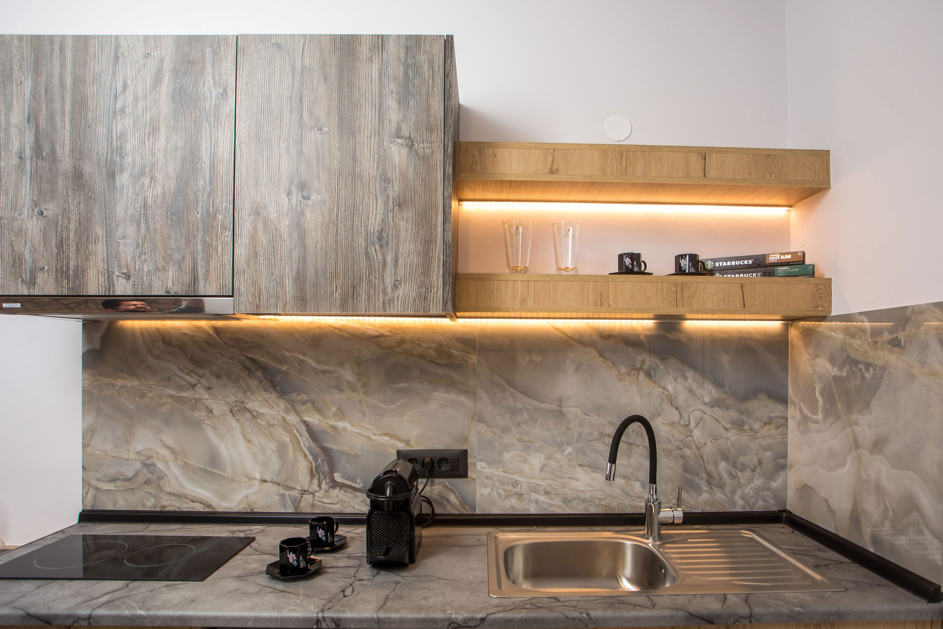 Een moderne keuken met een inbouwfornuis, een spoelbak, houten kastjes en een marmeren spatwand.