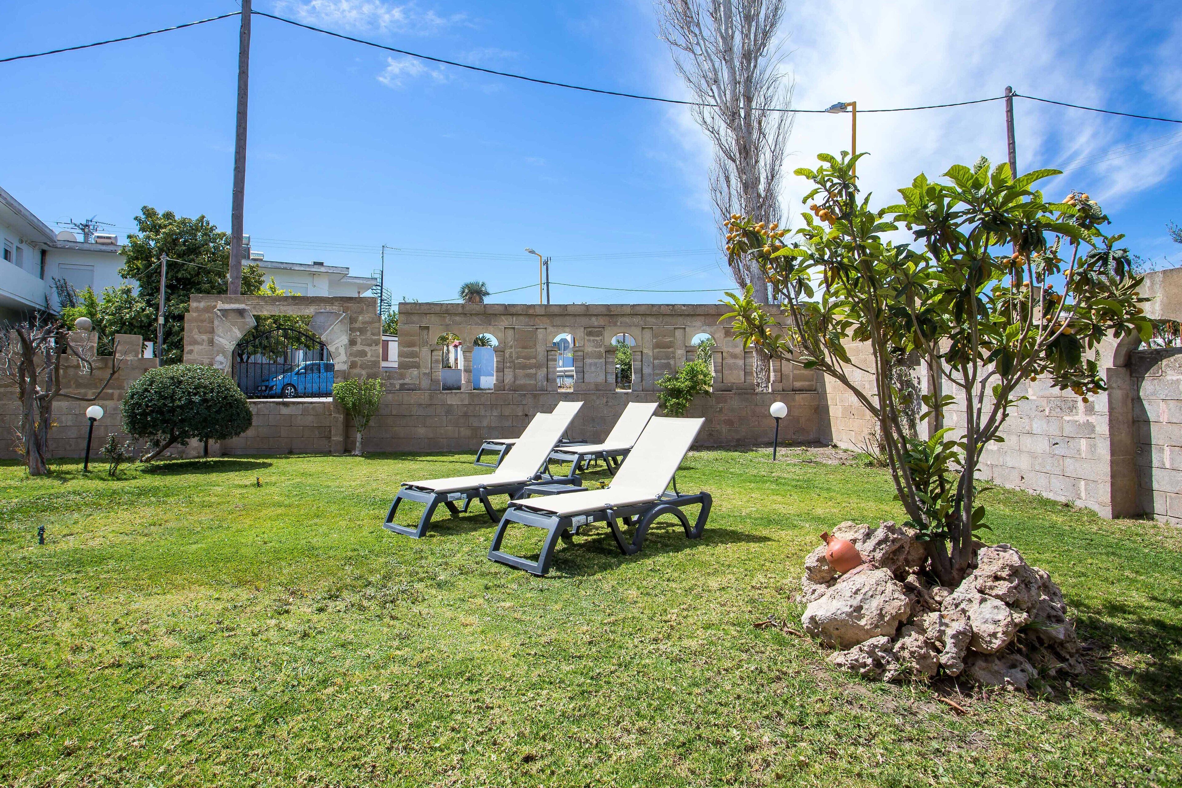 Une cour avec deux fauteuils de jardin blancs, un petit arbre et un mur en pierre.
