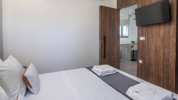 A hotel room with a bed, a TV mounted on the wall, and a mirror reflecting the bathroom.