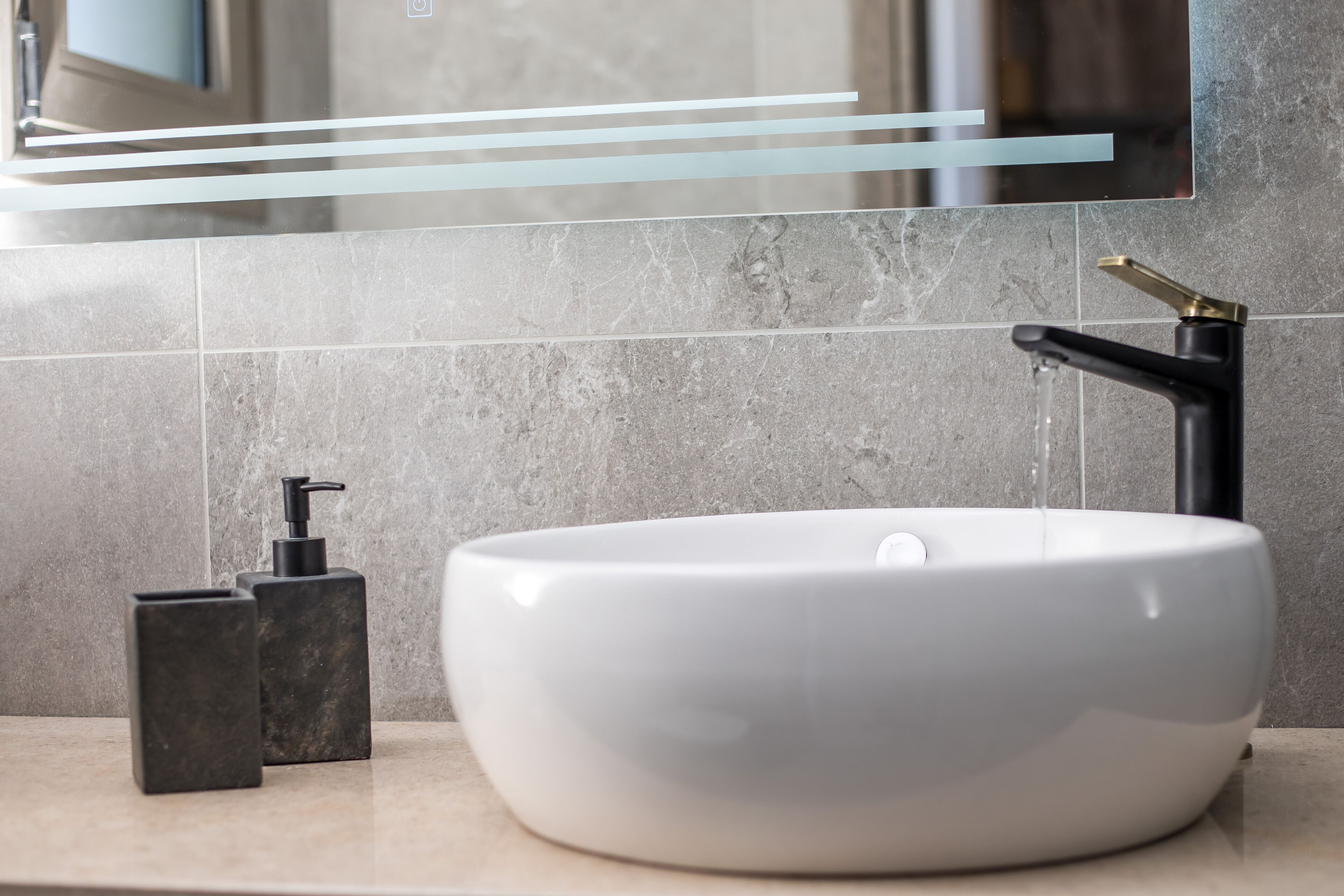 A bathroom with a white sink, black faucet, and black soap dispenser.